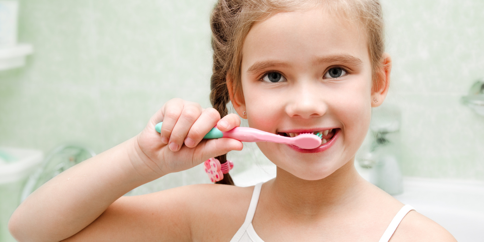 Smiling cute little girl brushing teeth in bathroom hygiene concept